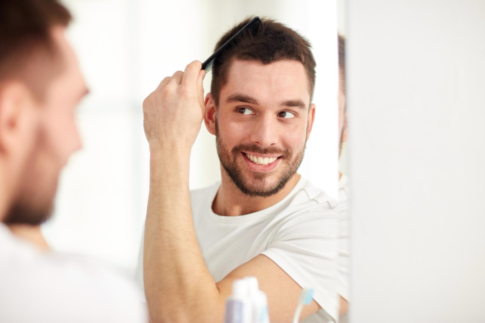 A man examining his hairline closely in a bathroom mirror while assessing early thinning